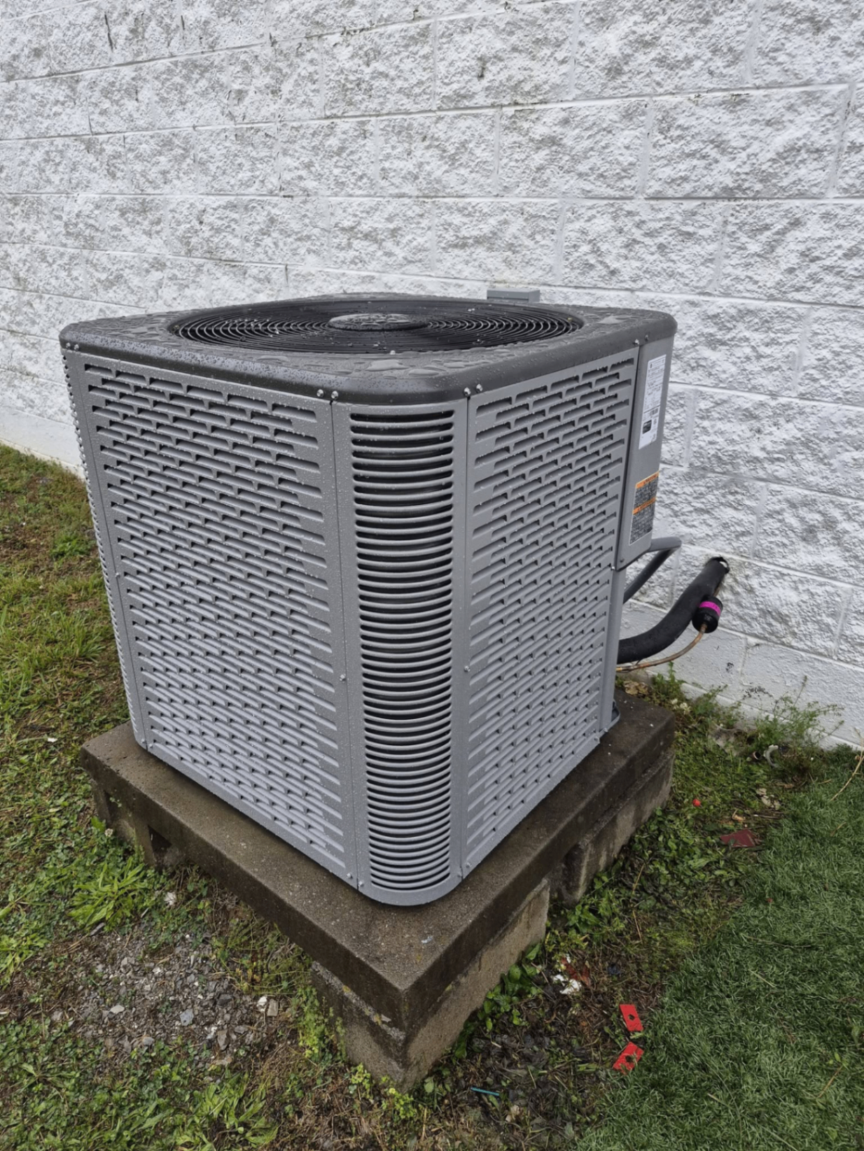 Outdoor condenser unit on concrete pad against block wall